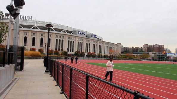 Runners race around Yancey Field with Yankee Stadium in the background