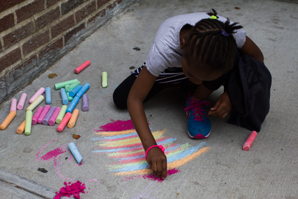 A child draws on the pavement with colored chalk outside Block 921. SAHELI ROY CHOUDHURY / The Bronx Ink