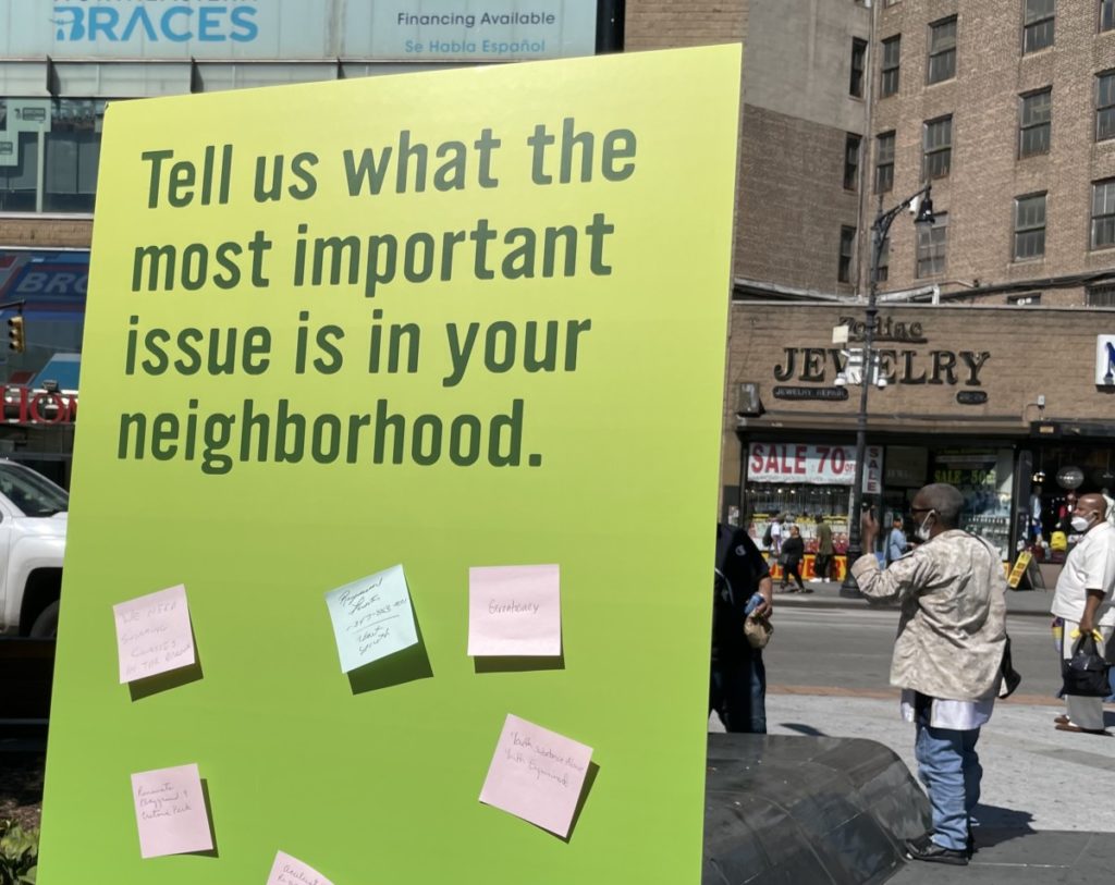 A poster board with the text "tell us what the most important issue is in your neighborhood" is covered in blue and pink sticky notes.